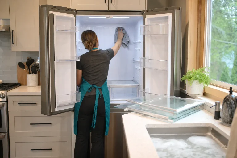 Cleaner in a teal apron wiping the inside of an emptied refrigerator in a Gresham kitchen